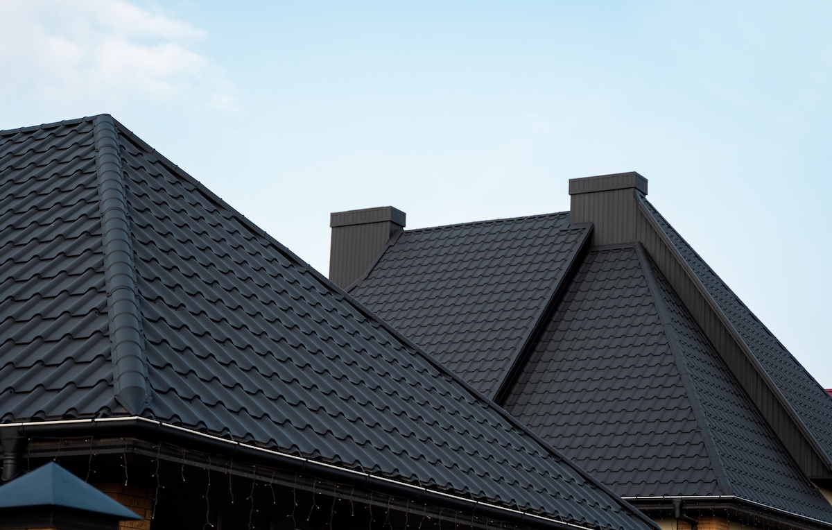 Several dark gray metal roofs with modern, clean lines and a tile pattern, set against a clear blue sky. These metal roofing East Greenbush NY installations feature prominent peaks and two rectangular vents or chimneys.