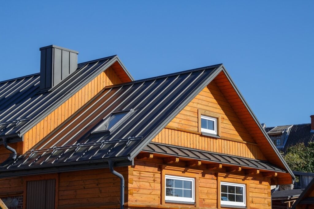 A wooden house with a gray metal roofing Delmar NY, multiple gables, and white-framed windows, set against a clear blue sky.
