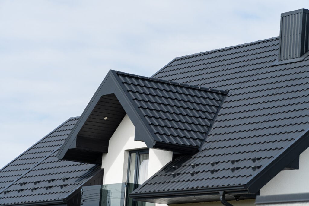 Close-up of a modern house with dark gray metal roofing Delmar NY and white exterior walls, featuring pitched roofs, a dormer window, and a clear sky in the background.