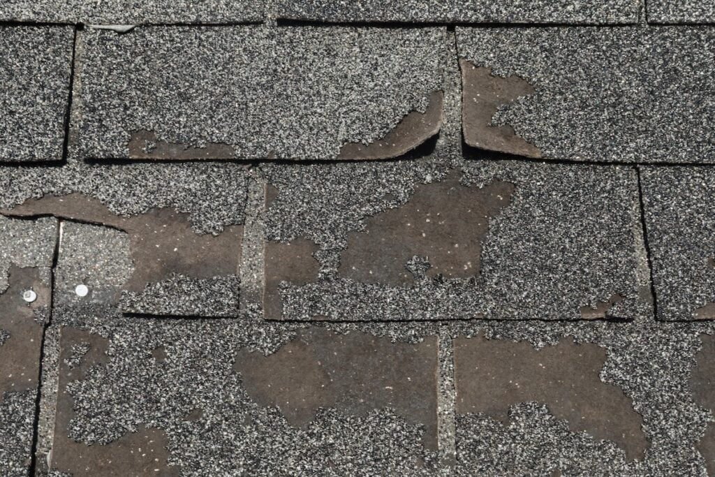 Close-up of damaged asphalt roof shingles with missing granules, curled edges, and visible nails, illustrating significant wear and common roof problems.