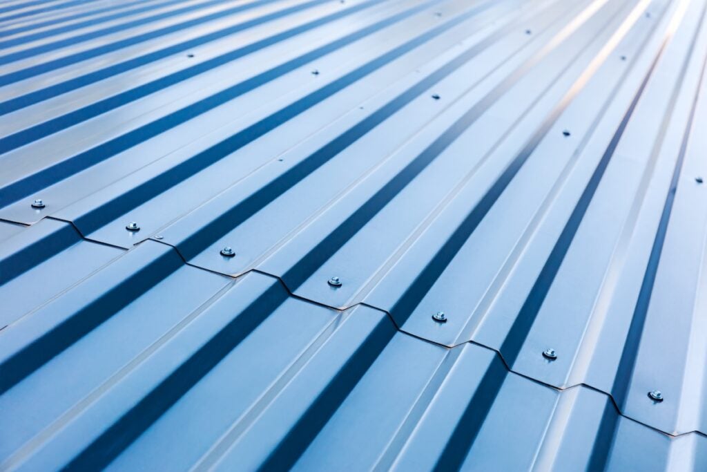 Close-up view of corrugated metal roofing in blue, with visible screws and shadows that highlight the wavy, ribbed texture.